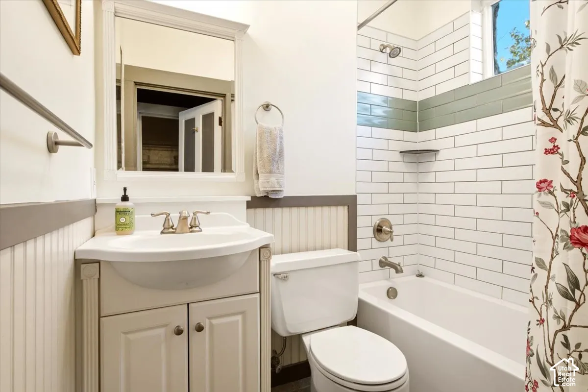 Bathroom featuring a pedestal-style vanity with an integrated sink, wainscoting detail, wall-mounted mirror, and a tub with a subway tile surround