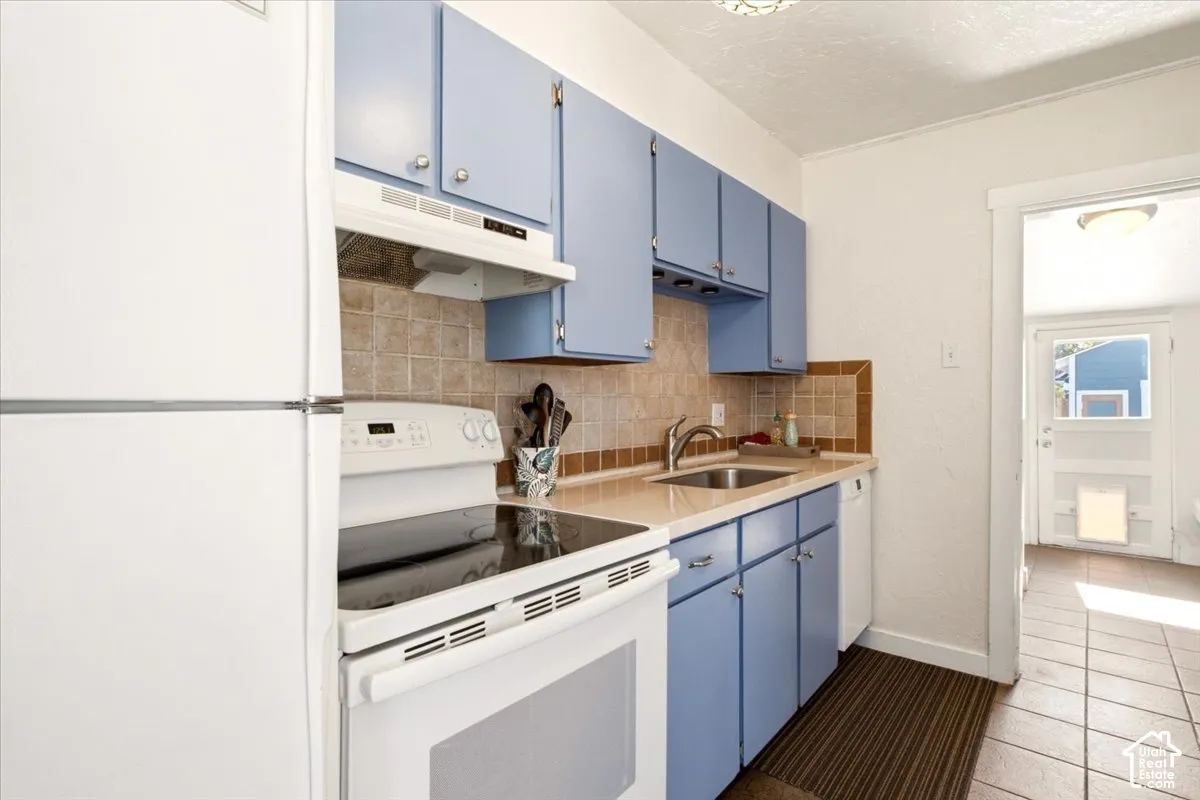 Kitchen featuring blue cabinetry, square tile backsplash, integrated range hood, white appliances (included)