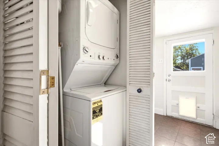 Stacked laundry unit housed in a closet with white louvered doors, tile flooring, and an exterior door featuring a built-in pet portal