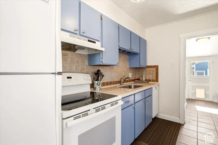 Kitchen featuring blue cabinetry, square tile backsplash, integrated range hood, white appliances (included)