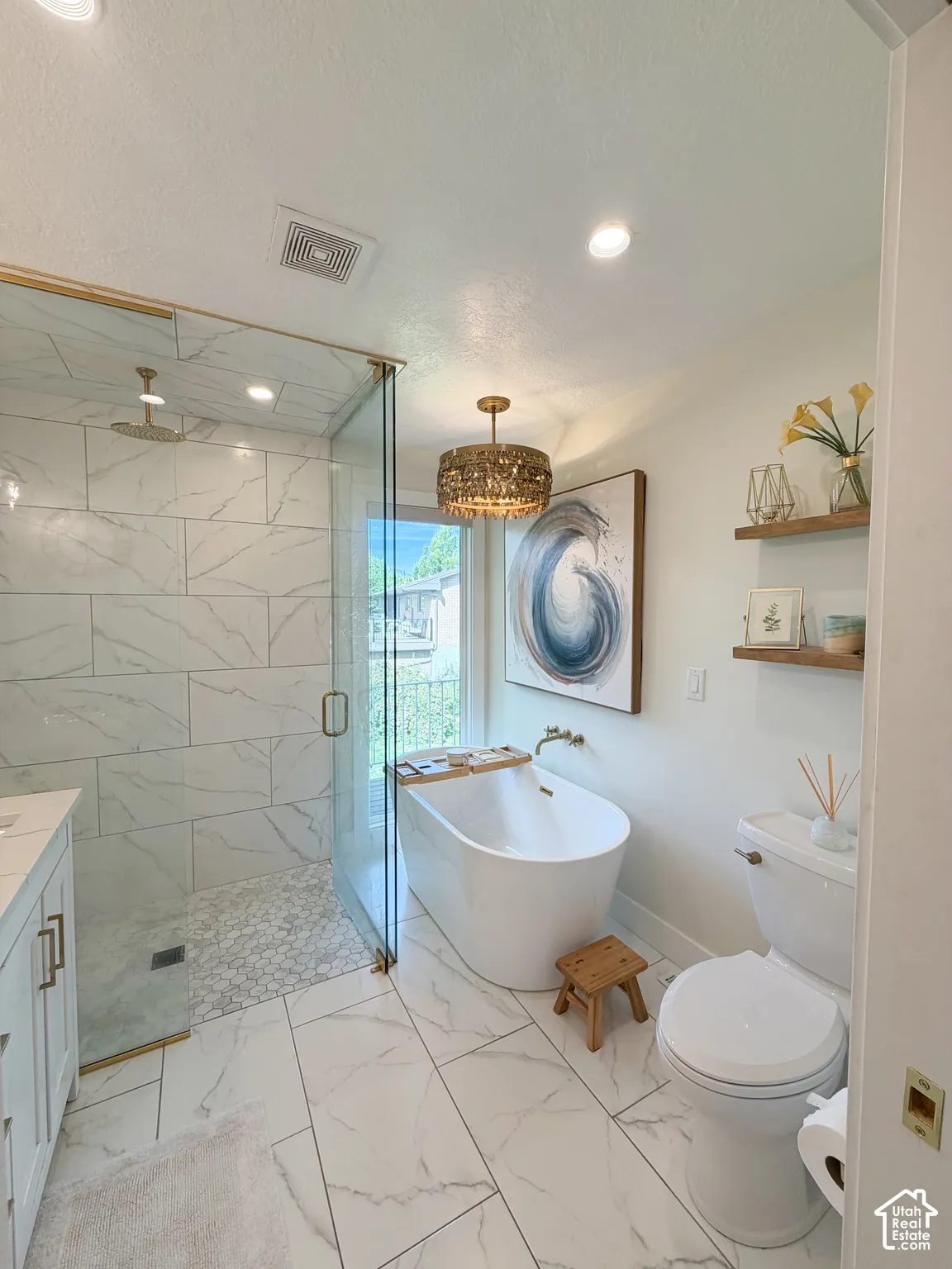 Walk-in shower with stone-tile surround, freestanding soaking tub, metallic drum pendant lighting, large-format tile flooring, and floating wall-mounted shelving