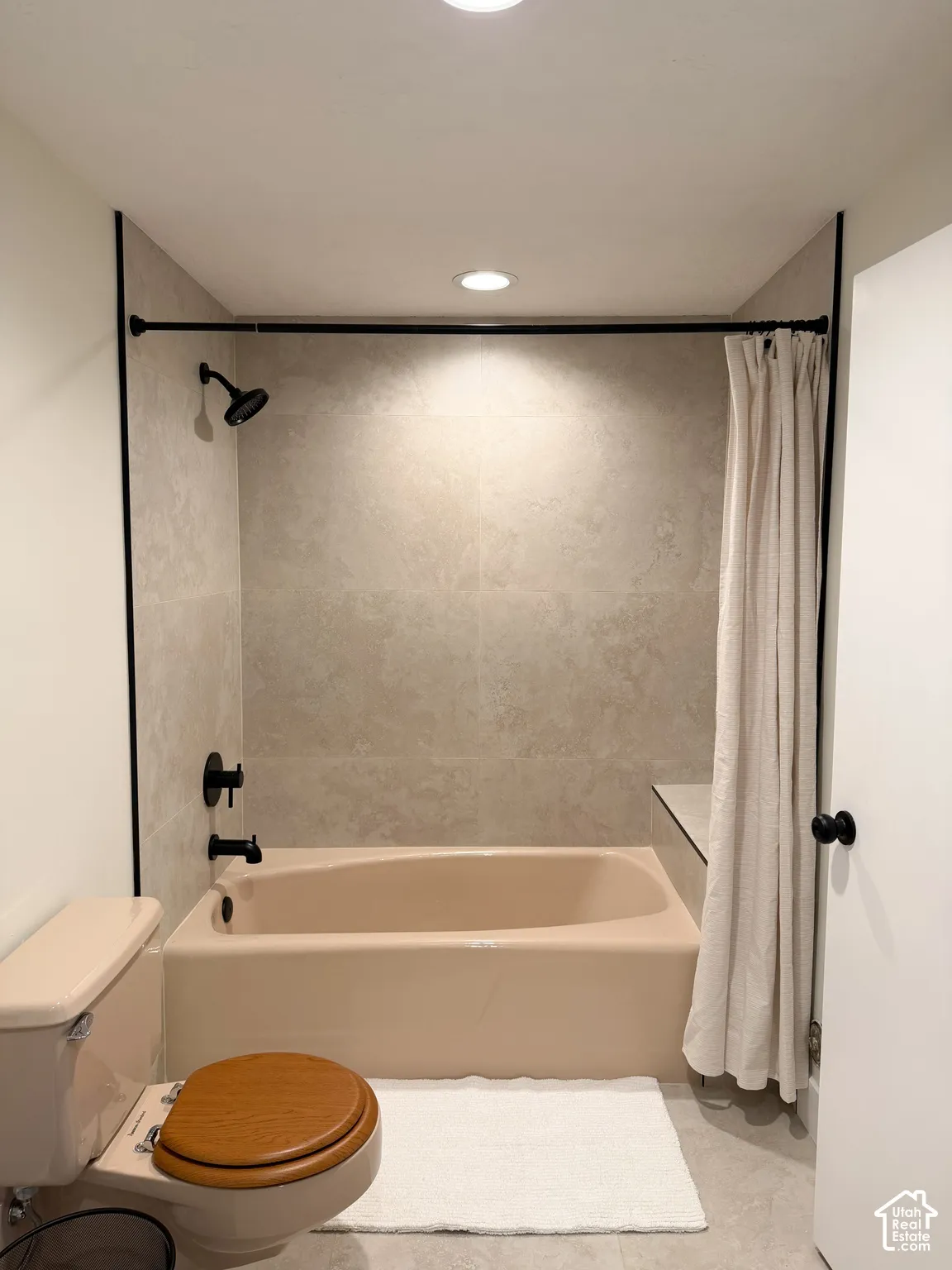 Bathtub area featuring large-format wall tile, matte black shower fixtures, and a recessed ceiling light