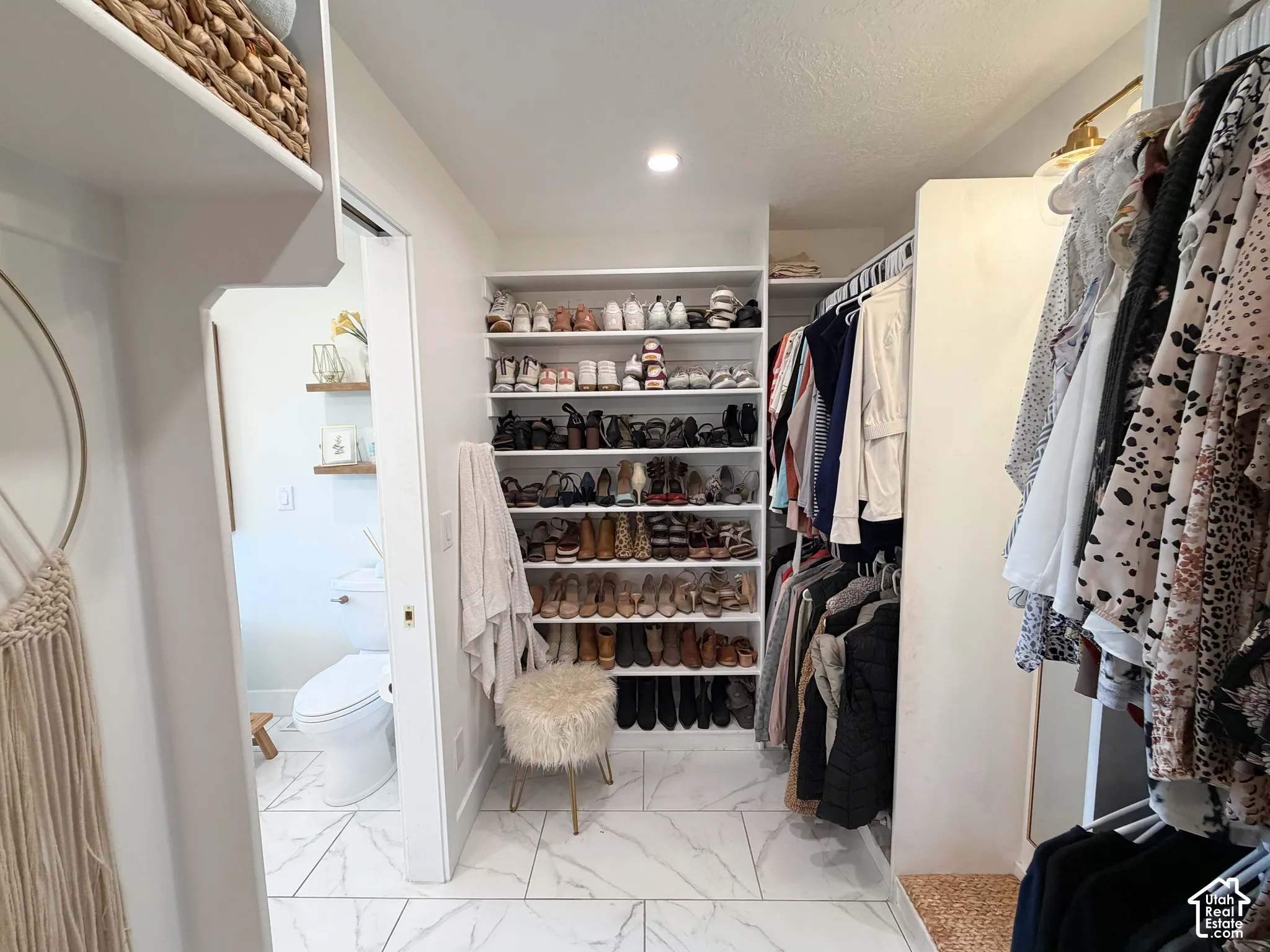 Walk-in closet featuring white built-in shelving, hanging rods, and large-format tile flooring