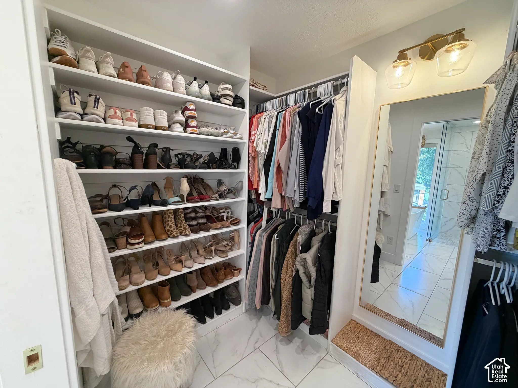 Custom walk-in closet featuring extensive built-in shelving, double-tiered hanging rods, stone-finish tile flooring, and integrated wall lighting