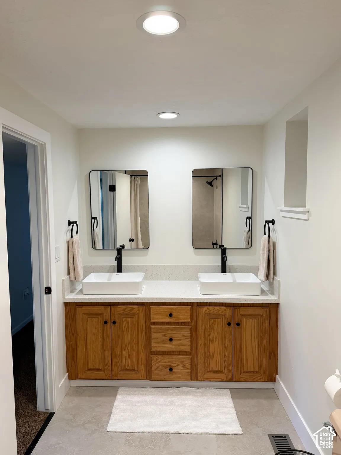 Double vanity featuring a light-toned countertop, rectangular vessel sinks, matte black widespread faucets, wood-finish cabinetry, and framed mirrors