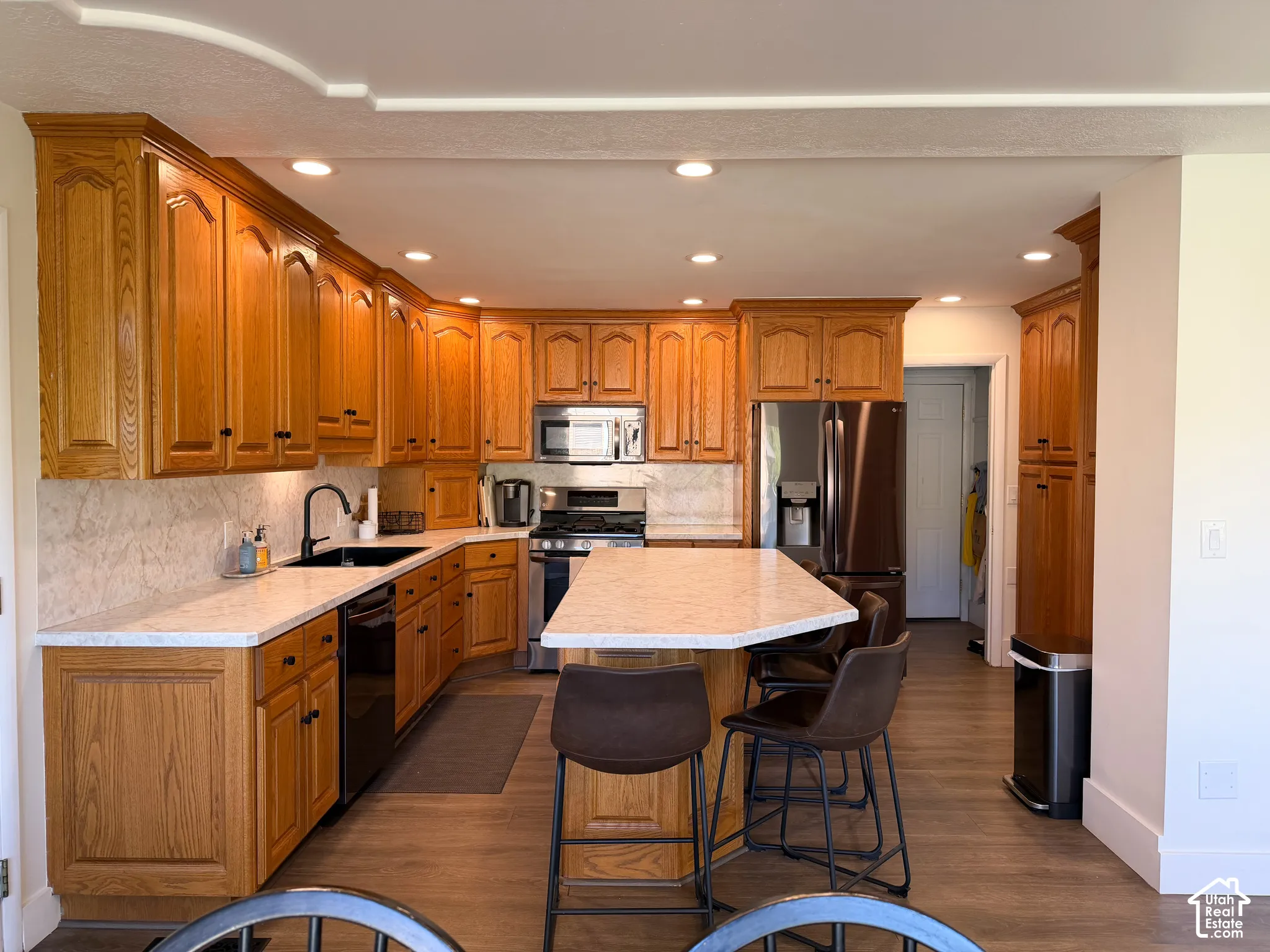 Kitchen featuring oak cabinetry, solid-surface countertops, center island with breakfast bar seating, stainless steel appliances, and recessed lighting