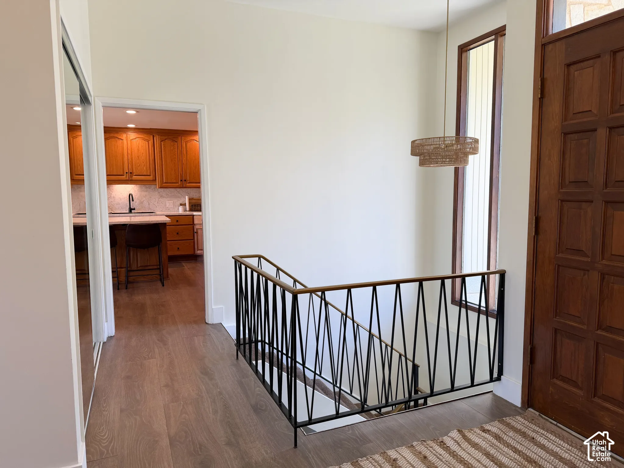 Entry featuring a solid wood panel door, geometric metal balustrade with a wood handrail, vertical fixed-pane window, and wood-finish flooring