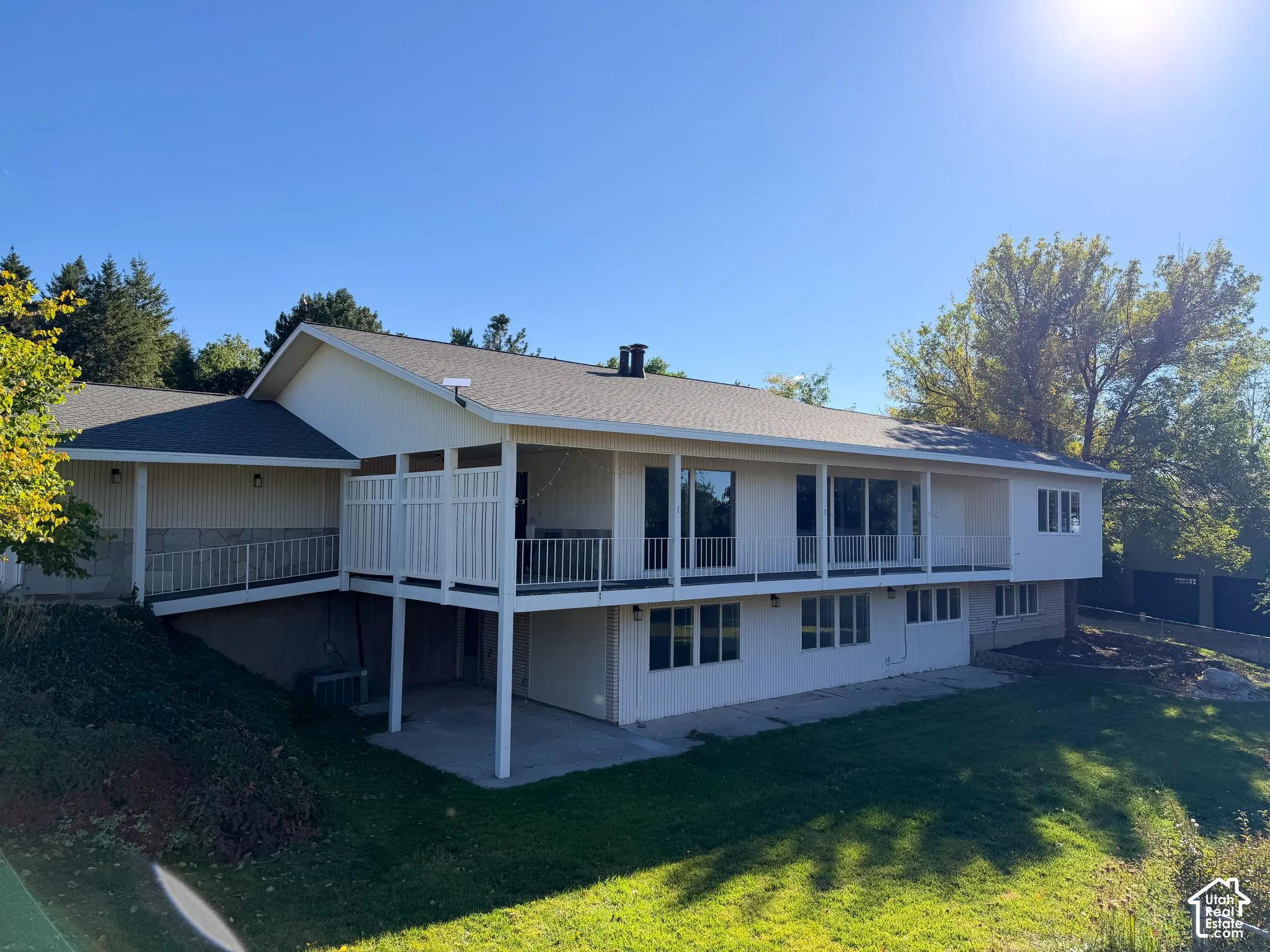 Exterior featuring a covered wrap-around deck, painted siding, a lower-level concrete patio, and a sloped lawn