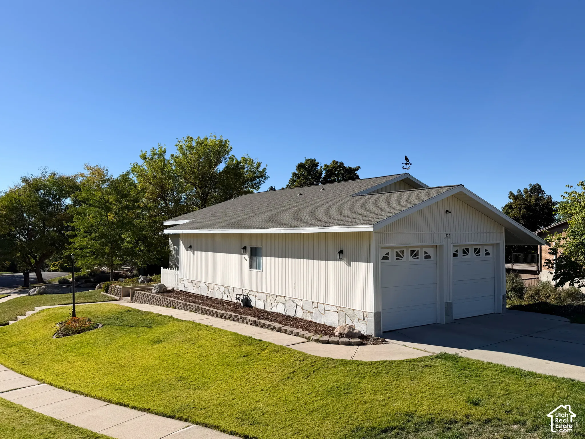Two-car garage featuring vertical siding, stone foundation detailing, asphalt shingle roofing, and an ornamental rooftop weather vane