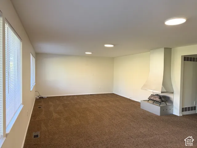 Spacious room featuring a metallic fireplace with a modern hood, wall-to-wall carpeting, multiple flush-mount ceiling lights, and large windows with horizontal blinds