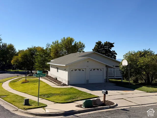 Corner lot exterior featuring a two-car garage, stone masonry skirting, covered porch, and concrete driveway
