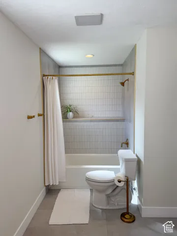 Bathroom featuring a tub-shower combination with floor-to-ceiling vertical tile, integrated recessed shelving, gold-tone hardware, and large-format neutral floor tile