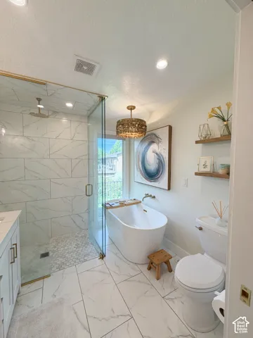 Walk-in shower with stone-tile surround, freestanding soaking tub, metallic drum pendant lighting, large-format tile flooring, and floating wall-mounted shelving