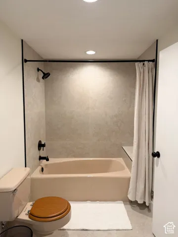 Bathtub area featuring large-format wall tile, matte black shower fixtures, and a recessed ceiling light