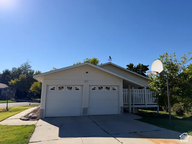 Exterior featuring light-toned metal siding, a two-car garage with decorative window inserts, an attached covered porch with railings, and a roof-mounted weathervane