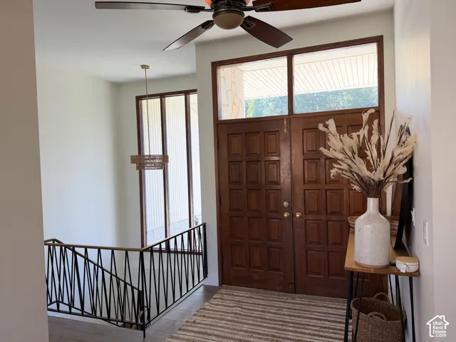 Double entry doors featuring raised panels and a transom window, geometric metal railing, large floor-to-ceiling windows, and a ceiling fan with integrated lighting