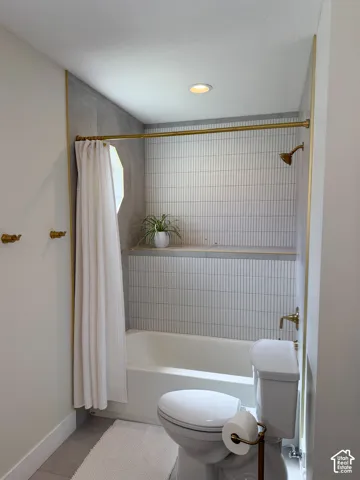Bathroom featuring a tiled tub surround with vertical white tile and a built-in ledge, brass-tone hardware, recessed ceiling lighting, and large-format floor tile