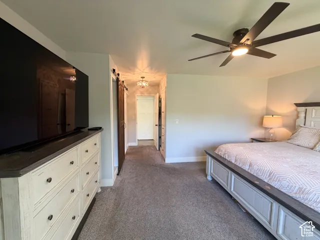 Neutral-toned interior featuring a ceiling fan with integrated lighting, wall-to-wall carpeting, and a sliding barn-style door