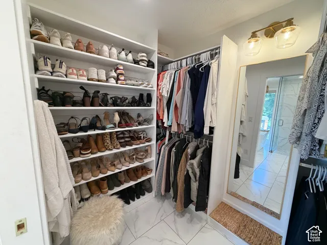 Custom walk-in closet featuring extensive built-in shelving, double-tiered hanging rods, stone-finish tile flooring, and integrated wall lighting