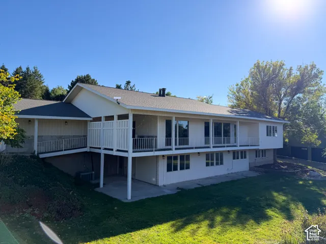 Exterior featuring a covered wrap-around deck, painted siding, a lower-level concrete patio, and a sloped lawn