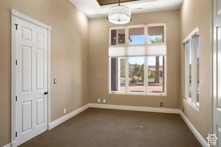Room featuring tall ceilings with recessed tray lighting, a multi-pane window configuration, neutral carpeting, and a modern drum-style pendant light fixture