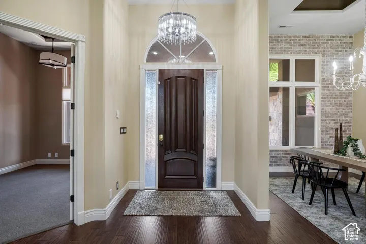 Entryway featuring a dark wood-finish door with sidelights and an arched transom window, wood-finish flooring, and a crystal chandelier