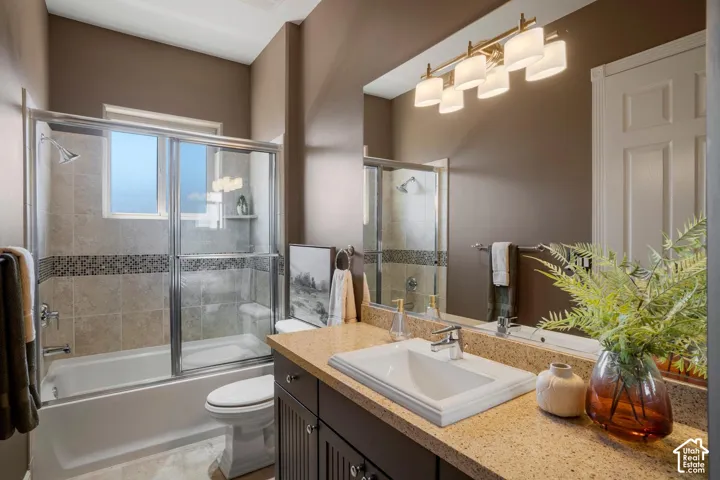 Bathroom featuring a vanity with a drop-in sink and stone-composite countertop, shower-tub combination with tile surround and mosaic inlay, large wall-mounted mirror, and multi-bulb vanity lighting