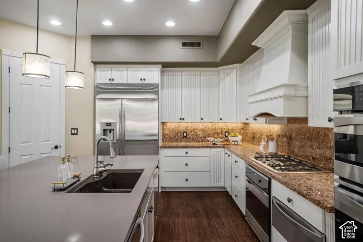 Kitchen featuring white cabinetry with beadboard detailing, stone-finish countertops, stainless steel appliances, a center island with an undermount sink, and wood-finish flooring