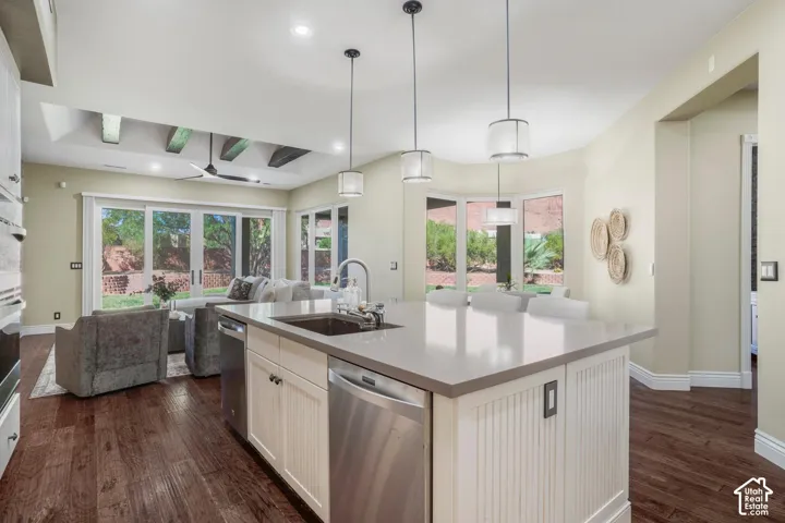 Kitchen featuring a central island with a quartz countertop, stainless steel appliances, wood-finish flooring, recessed ceiling beams, and pendant lighting