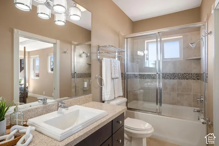 Bathroom featuring a vanity with a stone-finish countertop, undermount sink, multi-light fixture, and a tub-shower combination with decorative tile inlay and chrome hardware