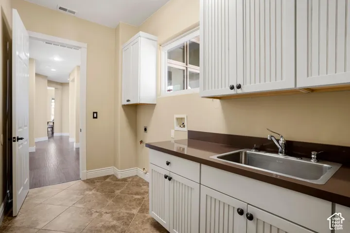 Laundry room featuring white beadboard cabinetry, solid-surface countertops, a stainless steel drop-in sink, and tile flooring