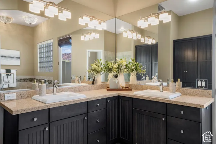 Dual-sink vanity featuring dark-toned cabinetry with beadboard detailing, stone-composite countertop, full-width wall mirror, and integrated lighting fixtures