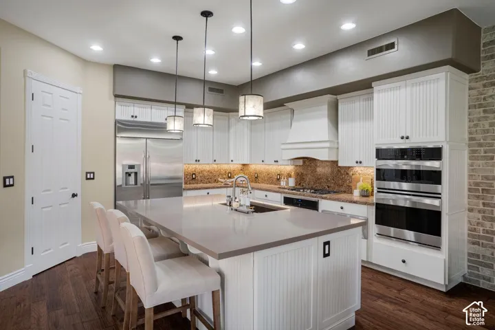 Kitchen featuring white cabinetry with beadboard detailing, expansive center island with stone countertop, stainless steel double wall ovens, recessed lighting, and wood-finish flooring