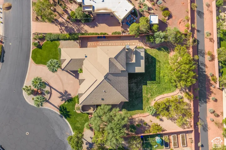 Aerial perspective of a corner lot property featuring a multi-gabled tile roof, a paved circular driveway, expansive lawn areas, mature perimeter landscaping, and elevated garden beds