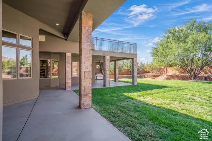 Covered concrete patio featuring stone-clad support columns and an elevated metal railed balcony