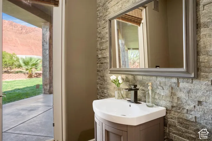 Stacked stone accent wall, white ceramic basin, dark-finish single-handle faucet, and framed wall mirror with red rock mountain scenery