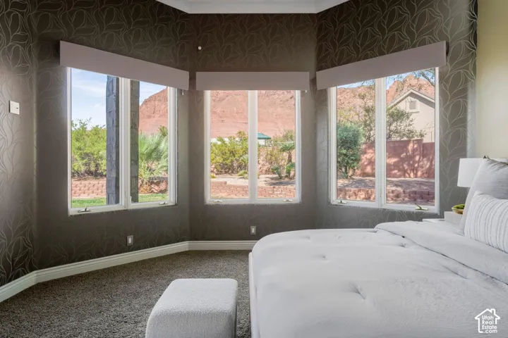 Bay window featuring three large windows, patterned wall covering, neutral carpeting, and rock formation scenery