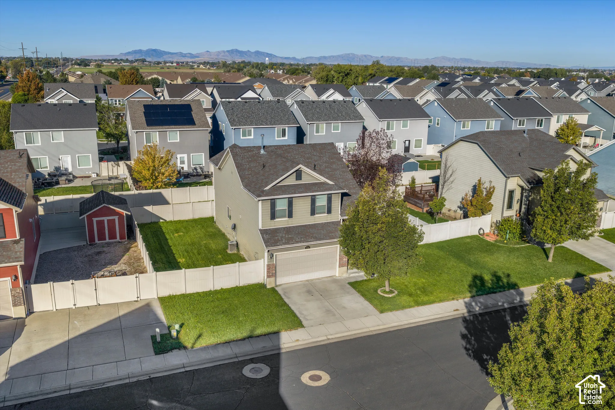 Two-story residence featuring a shingled roof, attached two-car garage, fenced yard, and mountain backdrop