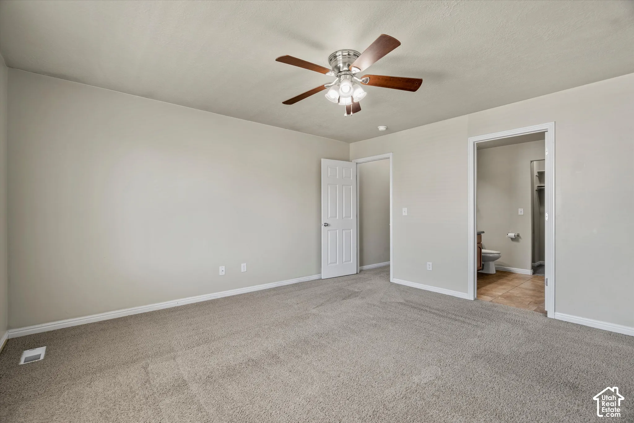 Neutral interior featuring wall-to-wall carpeting, a multi-blade ceiling fan with integrated lighting, and a six-panel interior door