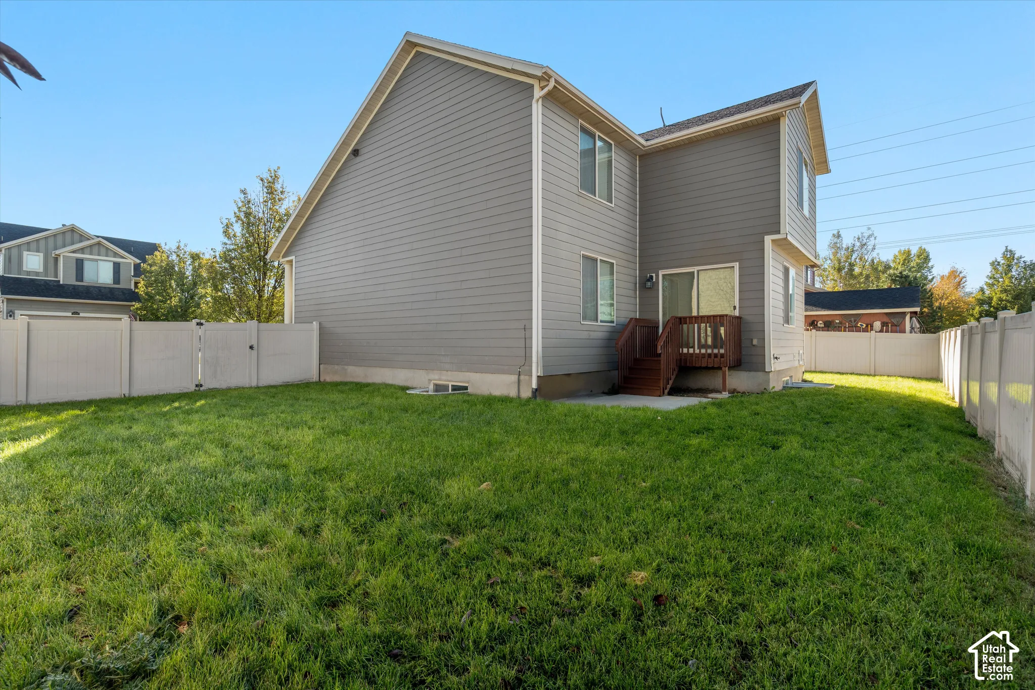 Rear exterior featuring gray horizontal siding, a fenced perimeter, a concrete patio, and a raised wood-finish deck with stairs