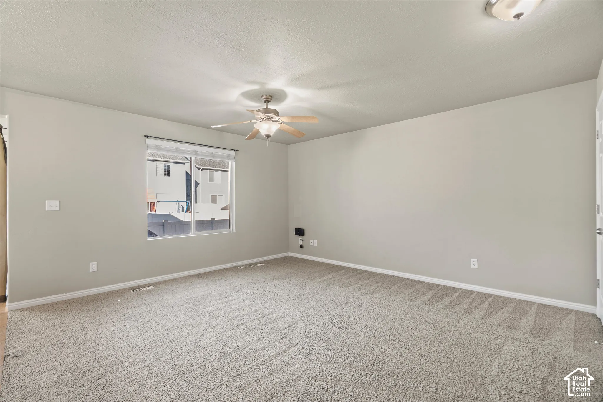 Neutral-toned interior space featuring wall-to-wall carpeting, a multi-blade ceiling fan with integrated lighting, and a single-pane window
