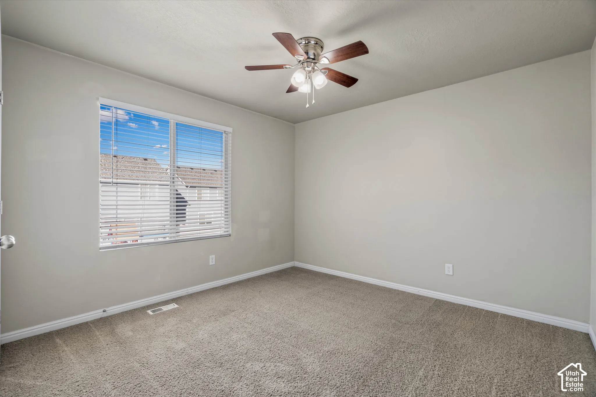 Neutral-toned interior featuring wall-to-wall carpeting, a multi-blade ceiling fan with integrated lighting, and a large window with horizontal blinds