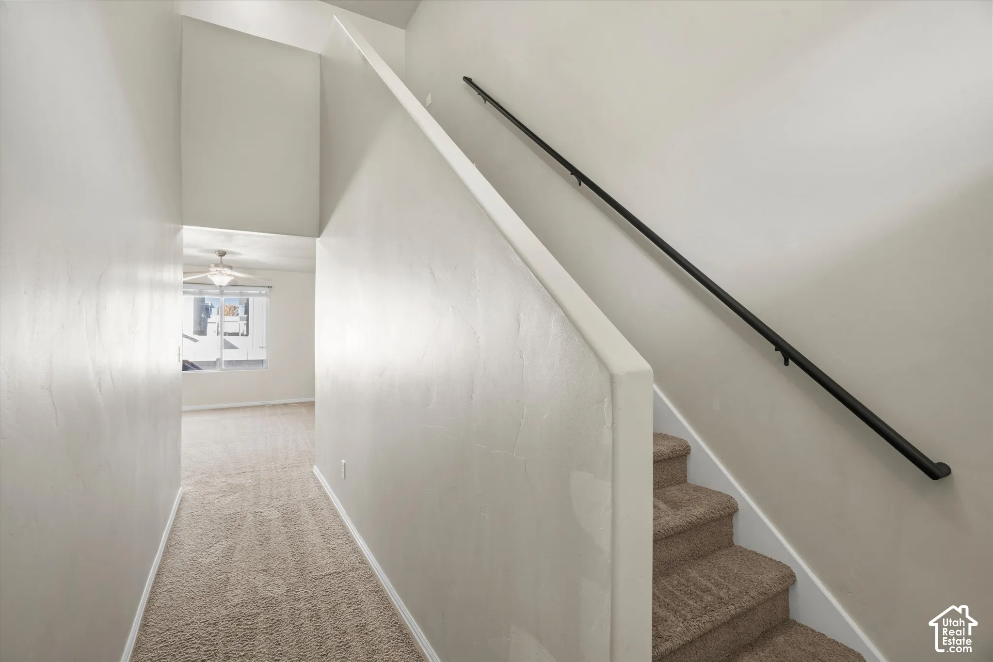 Interior staircase featuring neutral-toned carpeting, a solid wall railing, and a minimalist black metal handrail