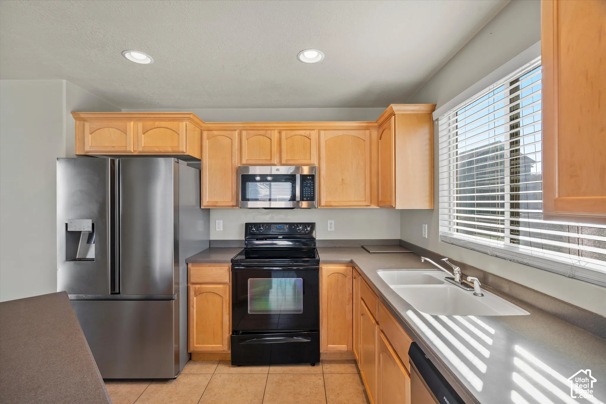 Kitchen featuring wood cabinetry, stainless steel refrigerator, microwave, black range, and white double-basin sink with tiled flooring