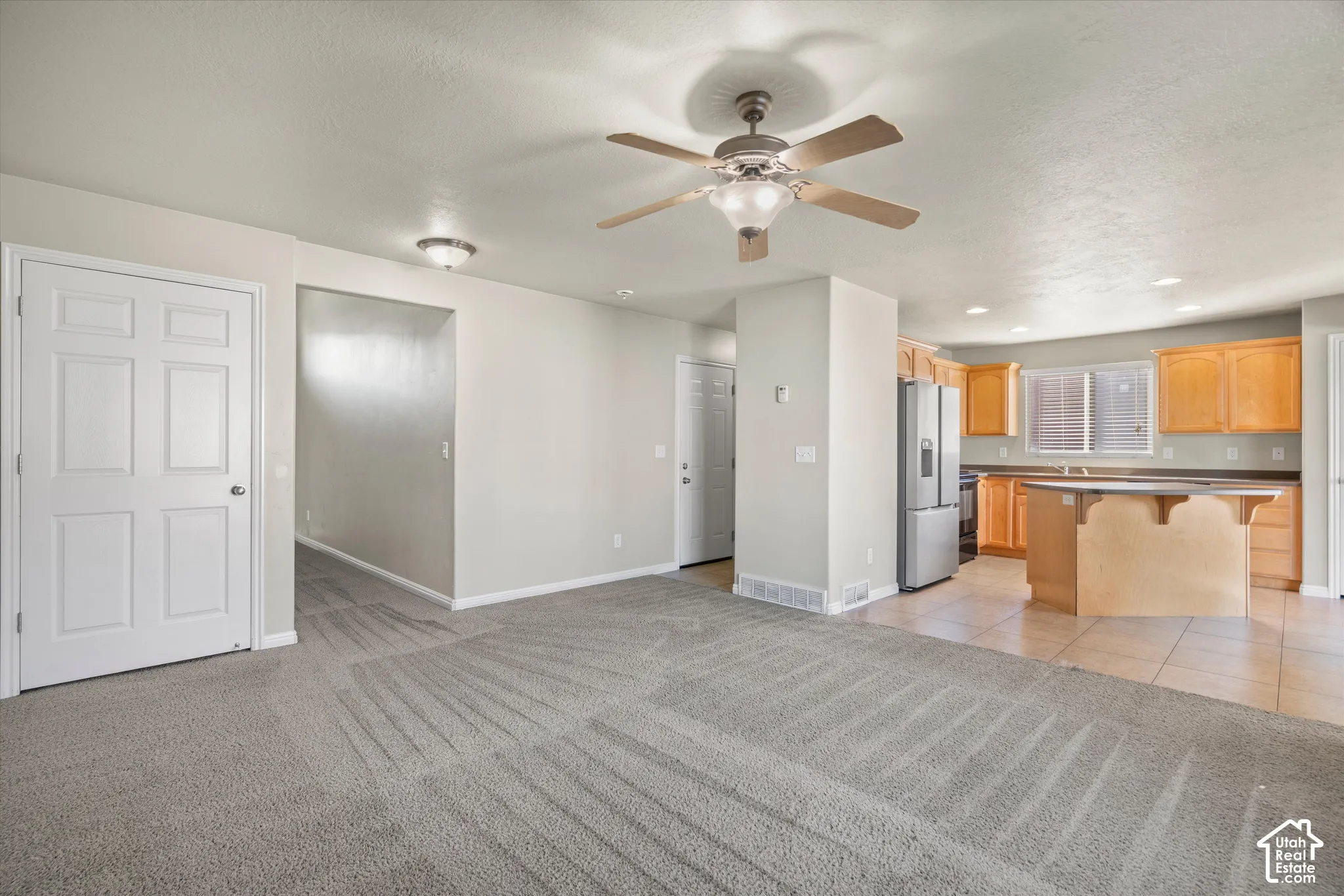 Interior space featuring neutral carpeting, a ceiling fan with integrated lighting, kitchen cabinetry, a kitchen island, and tile flooring