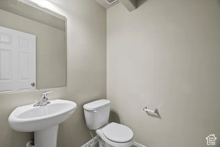 Wall-mounted frameless mirror above a white pedestal sink with chrome faucet and matching toilet