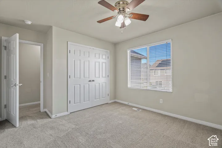 Neutral-toned interior room featuring carpeted flooring, a ceiling-mounted fan with integrated lighting, and white six-panel closet doors