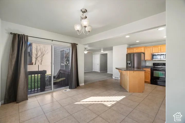 Kitchen featuring wood cabinetry, stainless steel appliances, and a central island, accompanied by tile flooring, recessed lighting, and a sliding glass door