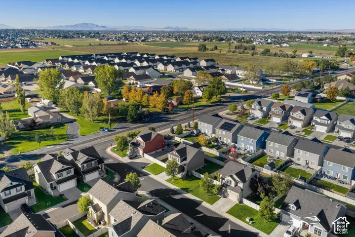 Aerial perspective of suburban residential neighborhood featuring asphalt paved streets, concrete driveways, residential homes with peaked rooflines, fenced yards, and mountainous horizon