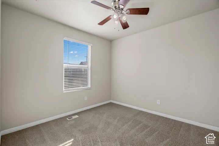 Neutral-toned interior space featuring wall-to-wall carpeting, a multi-light ceiling fan, and a single-pane window with horizontal blinds